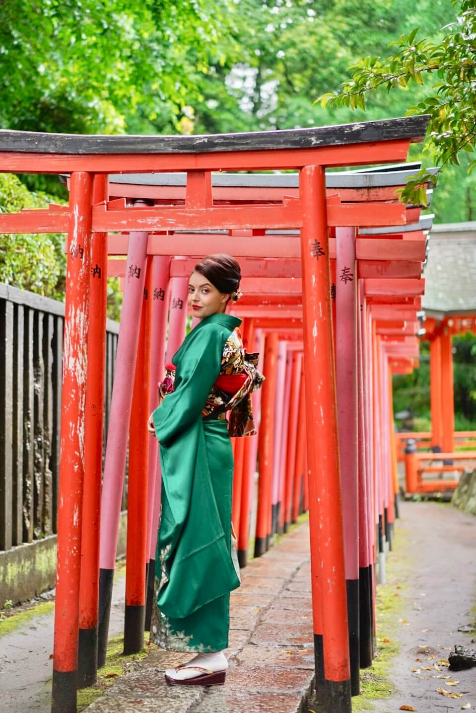 She walks through the torii gate tunnel at Nezu Shrine in a green kimono
